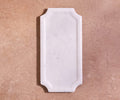 A Vivaen Framed Rectangle Board in White Marble with beveled edges rests on a light brown textured surface.