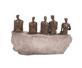 A brushed bronze Waiting Figure Statue features five abstract human figures seated closely together on a rough, stone-like base, all facing forward with elegantly elongated forms and minimal facial details. Subtle gold leaf accents highlight the contours of each figure, lending an elegant touch to the statue’s bronze finish.