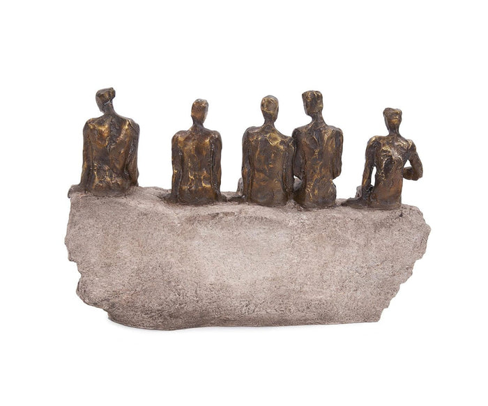 A brushed bronze Waiting Figure Statue features five abstract human figures seated closely together on a rough, stone-like base, all facing forward with elegantly elongated forms and minimal facial details. Subtle gold leaf accents highlight the contours of each figure, lending an elegant touch to the statue’s bronze finish.