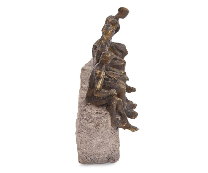 The “Waiting Figure Statue” is a bronze sculpture featuring abstract human forms sitting closely together on the edge of a textured stone block, viewed from the side, with delicate gold leaf accents highlighting their shapes.