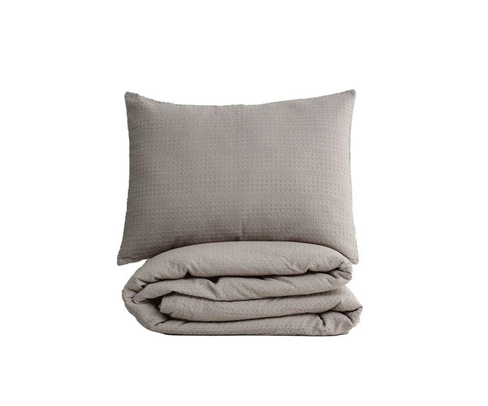 A neatly folded Woven Waffle Duvet Cover + Sham Set in Light Grey, crafted from soft cotton flax and inspired by minimalist Scandinavian bedding, with the matching sham placed in front—all displayed against a plain white background.